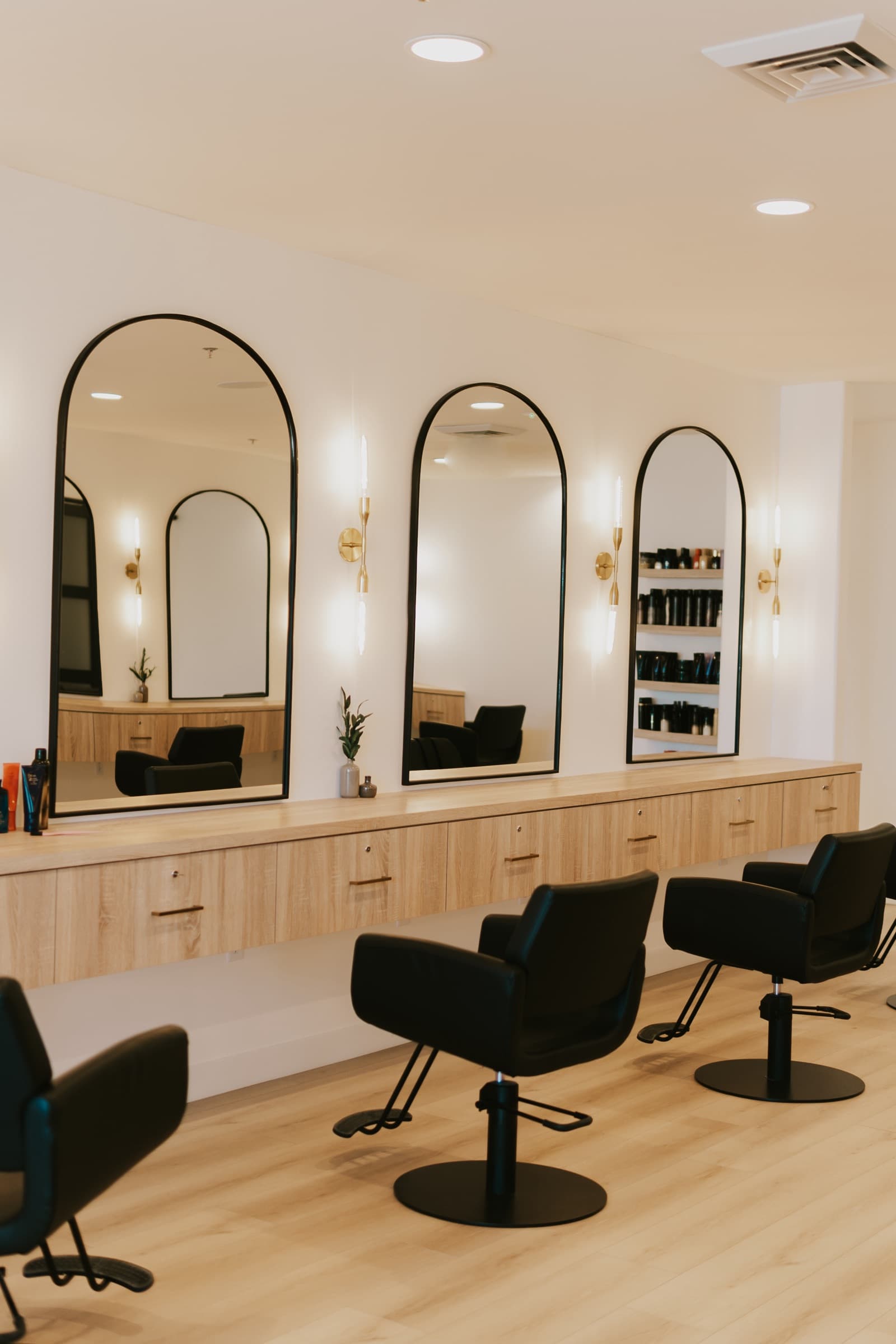 Three styling stations with arched mirrors, brass sconces and oak cabinetry.