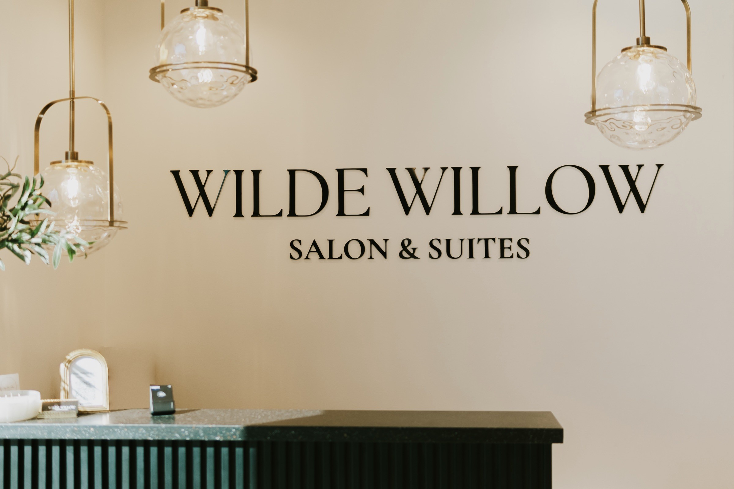 The Wilde Willow reception wall, with the salon's name in black lettering under brass and glass pendant lights.